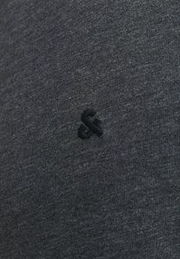 Mørk grå t-shirt lavet af blødt strikket stof. Har et lille, sort broderet logo på venstre side. Glat tekstur og enkelt design.