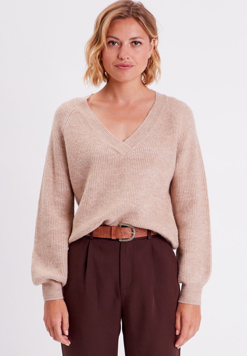 Beige strikket sweater med V-hals, ribbet tekstur og sænkede skuldre, parret med høj Talje brune bukser og et brunt bælte.
