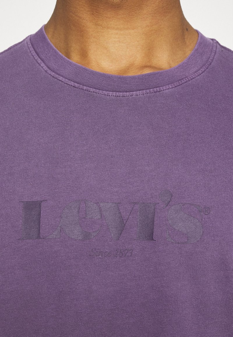 Camiseta de algodón morada con cuello redondo, mangas cortas y un prominente logo gris de Levi's impreso en el frente.