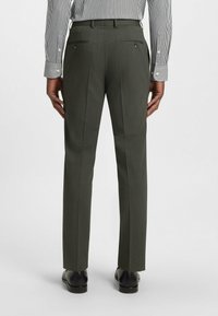 Green tailored trousers with a textured pattern, featuring double rear pockets and a slim fit, paired with black shoes. White striped shirt visible.