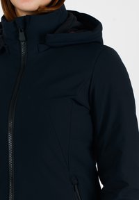 Giacca softshell blu navy con colletto alto, zip frontale e logo discreto sulla spalla. Tessuto liscio con un design aderente.