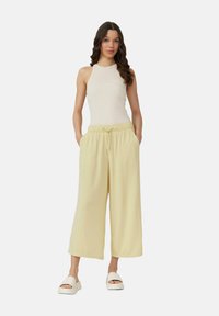 Lichtgele wijde broek met een elastische tailleband en trekkoord, gecombineerd met een aansluitend crèmekleurig tanktop en witte slip-on sandalen.