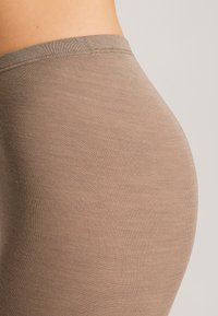 Hnědé žebrované legíny s hladkým povrchem a přiléhavým střihem, které mají široký pas a jemné švy.