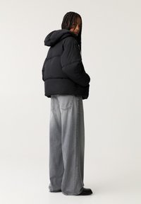 Giacca a vento nera con cappuccio, caratterizzata da una silhouette squadrata e sezioni cucite. Abbinata a jeans grigi a vita alta e dal taglio loose.