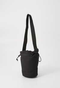 Black fabric crossbody bag with a drawstring top, adjustable strap, and front zip pocket. Features a cylindrical shape and soft texture.