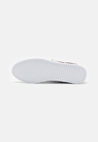 Semelle de baskets blanches avec des grooves et des rainures texturés. Bords renforcés et surface lisse, présentant un détail de marque subtil.