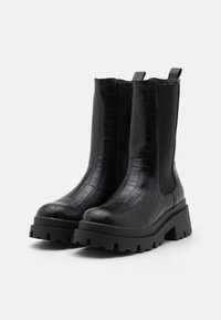 Bottes basses noires avec une texture crocodile, des panneaux latéraux élastiques et une semelle plateforme épaisse noire, dotées d'une languette pour un enfilage facile.