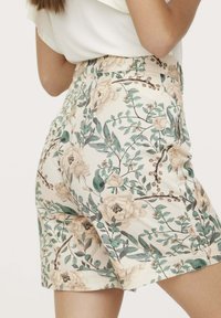 Shorts fleuris en tissu crème, présentant un motif de fleurs vertes et beiges. Comprend des poches latérales et un design de taille lisse.