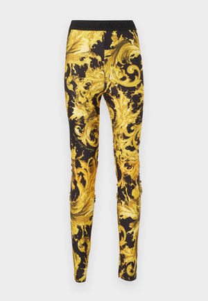 Leggings neri con ornamenti a motivi barocchi swirl in giallo brillante e oro, e una fascia in vita nera con testo.