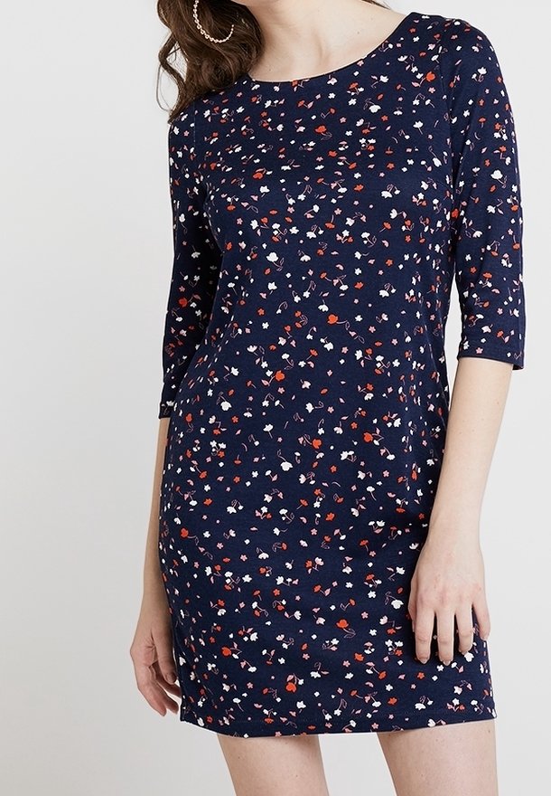Robe bleu marine avec motif floral rouge, blanc et rose, manches trois-quarts et encolure ronde portée par une personne debout.