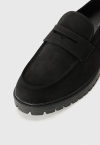 Schwarze Wildleder-Slipper mit dekorativem Vorderband und texturiertem Boden, runder Zehenpartie und starker Plateausohle.