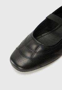 Černá kožená bota s kulatou špičkou. Obsahuje prošívaný vzor na vrchní části a široký elastický pás pro bezpečné uchycení. Hladký povrch.
