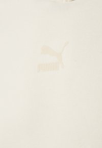 Sweatshirt couleur crème avec un logo Puma en relief beige clair texturé sur la poitrine. Tissu doux et lisse avec un design décontracté.