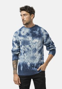 Gebreide trui in blauwverloop met kabelpatroon, voorzien van een ronde halslijn en ribgebreide mouwen. De stof heeft een zachte textuur.
