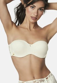Soutien-gorge sans bretelles couleur crème avec un tissu lisse, des bonnets moulés et des accents en dentelle sur les côtés ; présente un petit détail en métal de marque.