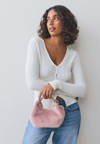 Valge tekstuuriga kampsun, heleroosa karvane käekott lühikeste sangadega ja sinised teksad. Lihtne disain, pehmed materjalid ja lõõgastunud vorm.