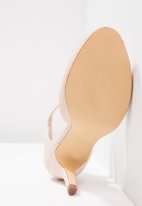 Jasnoróżowy but na wysokim obcasie z teksturowaną cholewką, spiczastym noskiem i smukłym obcasem. Podeszwa ma wzór kwiatowy.