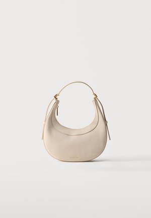 Sac à main en cuir beige en forme de croissant avec une sangle courte, des ferrures dorées et un petit tire-zipper, posé sur un fond clair uni.