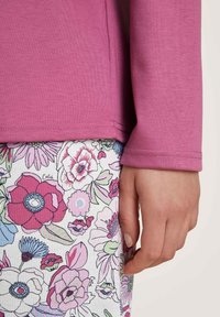 Roze long-sleeve top met een gladde textuur, gecombineerd met een rok met bloemmotief in roze, paars en groene elementen.