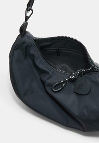 Borsa in tessuto nero e morbido, con una forma arrotondata e chiusura con zip. Presenta un'etichetta a forma di cuore nera e una tracolla resistente con una linguetta di presa testurizzata.