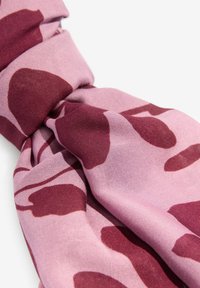 Bufanda rosa con formas orgánicas en color burdeos, que muestra una textura suave y un nudo suelto en un extremo para drapear, hecha de tejido ligero.