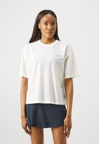 Tricou sportiv cu mânecă scurtă, fabricat din material tip plasă respirabil, având un decolteu rotund și un logo mic de culoare mov pe piept.