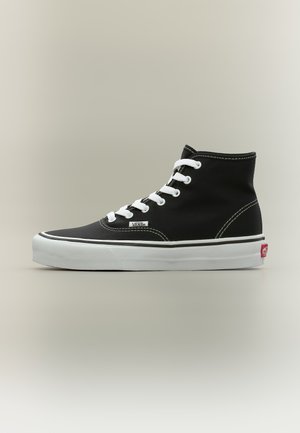 Μαύρο ψηλό καμβά Vans sneaker με λευκά κορδόνια, λευκή σόλα και κόκκινο λογότυπο στη φτέρνα, εμφανίζεται σε πλευρικό προφίλ σε ουδέτερο φόντο.