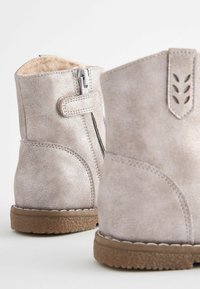 Stivali alla caviglia in oro rosa con finitura simile alla suede, chiusura con zip e rivestimento interno morbido. Suola texturizzata per grip e supporto.