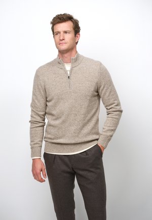 Beige, textured sweater with a quarter-zip collar, worn over a cream shirt, paired with dark gray, tailored trousers. Close-fitting design.
