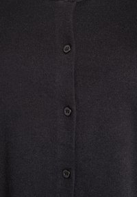 Schwarzer Cardigan aus strukturiertem Strickstoff mit glatter Oberfläche, der vorne mit einer Reihe von fünf schwarzen Knöpfen versehen ist.