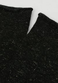 Svart stickad tyg med en strukturerad yta, som har silverprickar och en design med V-ringning. Kanten är ofullständig och lätt krullad.