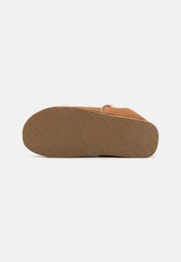 Pantofola in camoscio tan con suola piatta in gomma caratterizzata da una presa testurizzata e logo del marchio in rilievo, che mette in risalto una punta rotonda e un design semplice.