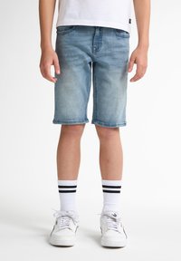 Shorts in denim dal lavaggio chiaro, che arrivano appena sopra le ginocchia, con un classico design a cinque tasche. Indossati con calzini bianchi con strisce nere e sneakers.