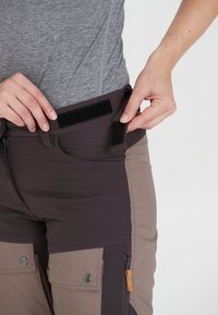 Donkergrijze en lichtbruine broek met een slim fit ontwerp, voorzien van klittenband op de taille en cargozakken met ritsen aan de zijkant.
