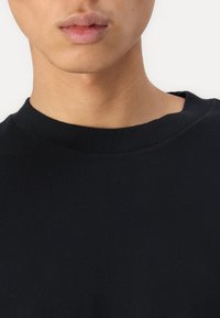 T-shirt in cotone nero con scollo rotondo. Il tessuto appare morbido con una finitura leggermente strutturata, enfatizzando un design classico.