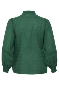 Groene blouse van een gestructureerde stof, met een geraffineerde halslijn, opgeblazen mouwen en kanten afwerking op de manchetten. Subtiel stippenpatroon.