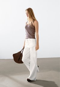 Bruine fitted tanktop gecombineerd met witte wijde broek. Het model draagt een gestructureerde bruine boodschappentas en heeft platformsandalen aan.