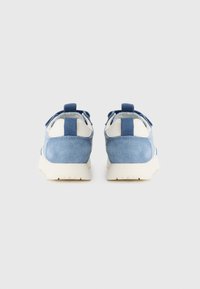 Baskets en suede bleu avec des accents blancs, forme arrondie, surface texturée et languettes à l'arrière pour un enfilage facile.