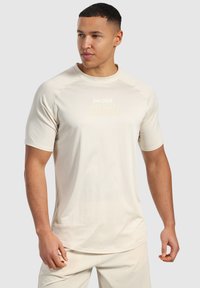 Ljust beige träningsskjorta i andningsbart, strukturerat tyg, med en logotyp på bröstet. Kortärmad och med rund halsringning.