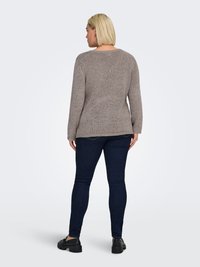 Brown knitted sweater with a round neck, long sleeves, and textured pattern, paired with dark blue skinny jeans and black footwear.