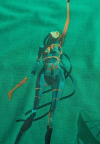 Groene T-shirt met een digitale illustratie van een figuur die naar boven reikt, met geometrische patronen en lijnen in donkere tinten die in elkaar verweven zijn.