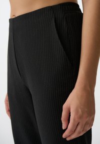 Pantaloni neri a righe sottili realizzati in tessuto intrecciato, con tasche laterali, una texture liscia e una vestibilità su misura. La vita si trova sui fianchi.