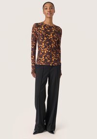 Langärmliges Oberteil im Leopardenmuster mit braunen, orangefarbenen und schwarzen Farbtönen. Kombiniert mit schwarzen, weiten Hosen und spitzen Schuhen.