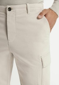 Beige cargobroek met een slim fit, frontzakken en een knoopsluiting. Zachte katoen met subtiele textuur en stikseldetails.