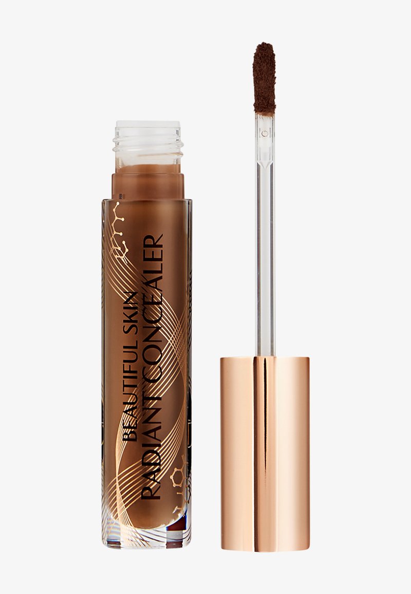Correcteur liquide marron dans un tube transparent avec des accentuations dorées. Présente un applicateur en forme de fluffy pour une application précise.