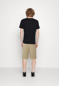Černé bavlněné tričko a khaki šortky, volný střih. Model má na sobě černé vysoké tenisky. Jednoduchý design, žádná viditelná loga ani vzory.