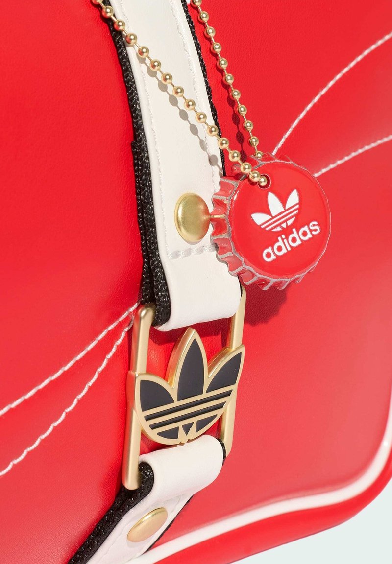 Red bag with white and black trim features a gold and black Adidas trefoil buckle and a red Adidas bottle cap keychain on a gold chain.