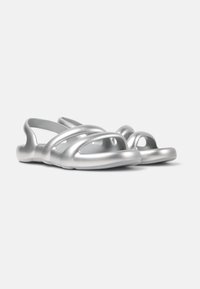 Silver sandals with a smooth, shiny finish, featuring multiple wide straps and circular openings on the sides for ventilation.