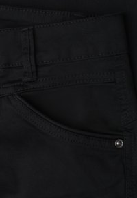 Jean en denim noir en gros plan montrant la poche avant, la boucle de ceinture et le détail des rivets métalliques.