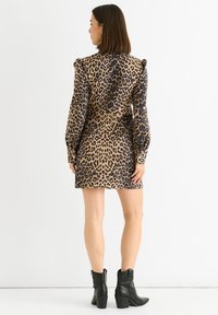 Woman standing facing backward wearing a leopard print long-sleeve mini dress with puffed shoulders and black ankle boots.
